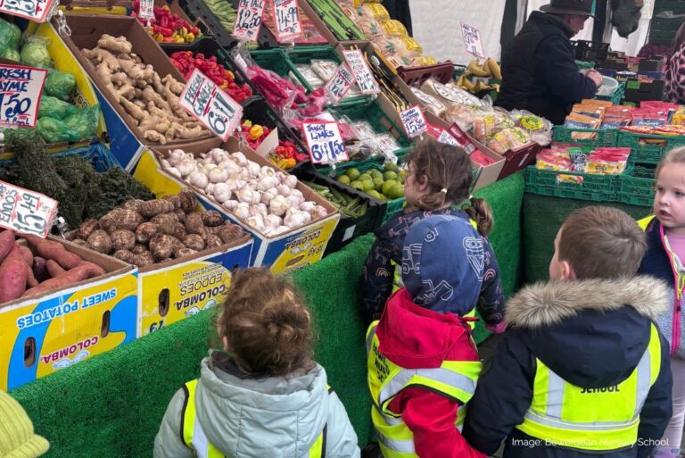 Young children at a market fruit and veg stall.